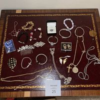 Full spread of assorted costume jewelry on a red leather patterned surface including a watch, rings, bracelets, necklaces, and brooches.