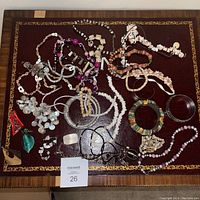 Top view of assorted costume jewelry including necklaces and bracelets spread on a maroon fabric surface with gold border detailing.