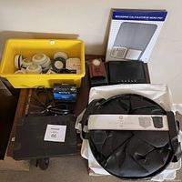 Overview of mixed electronics items including a yellow bin with speaker components, digital photo frame, Sony floppy disks, collapsible storage bin, and mousepad calculator