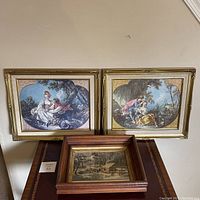 Three framed prints: two large Rococo style romantic scenes and one smaller rustic landscape print in wood and gold frame.