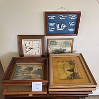 Overview of the stacked framed prints and the wall clock leaning against the wall