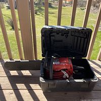 Red Homelite chainsaw inside black carrying case, shown from the side with bar extended.