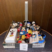 Box containing varied vintage Mickey Mouse plush toys, figurines, novelty items with bright colors and Disney branding
