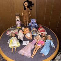 Full lot including various vintage dolls and Beanie Baby bear, laid out on a round table.