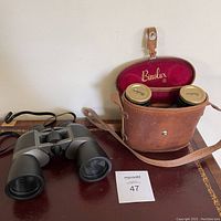 Vintage Binolux binoculars placed next to their brown leather carrying case with red velvet interior.