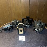 All five vintage cameras arranged on a tabletop against wood paneled wall