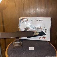 Photo of the vintage table lamp placed on a round table with wooden panel background, showing the lamp base and horizontal head.