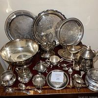 Photo of the entire silverware set including trays, bowls, teapot, spoons, and serving utensils arranged on a wooden surface.