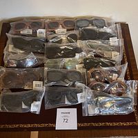 Photo showing 19 individually packaged new women's sunglasses in various frame shapes and colors on a table.