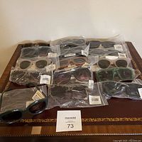 Full lot of 12 pairs of new women's sunglasses on a table, each still in plastic wrapping.