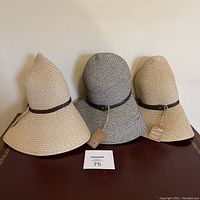 Three women's sun hats displayed side by side on a surface against a wall, showing their conical shape and braided decorative bands.