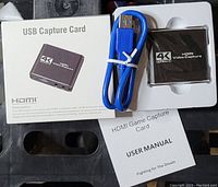 Photo of the Tkhin 4K HDMI USB capture card in packaging including box, blue USB 3.0 cable, and user manual.