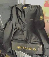 Photo of black Ptahdus heated jacket showing folded jacket with zipper and branding on sleeve and hem.