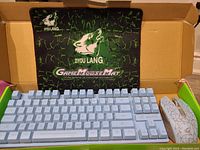 Photo showing white wireless gaming keyboard, cracked pattern gaming mouse, and branded Ziyou Lang Game Mouse Mat inside the packaging box.