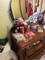 Photo showing vintage Coca-Cola bottles, pins, and glasses on a wooden dresser with a mirror in the background.
