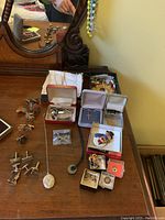 Wooden dresser top with various men’s cufflinks, tie clasps, boxed costume jewelry including porcelain flower earrings and brooch, and 10K gold class ring in several small boxes.