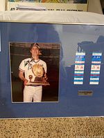Framed autographed photo of Dale Murphy in Atlanta Braves uniform holding a trophy with two game tickets and plaque on blue matte background.