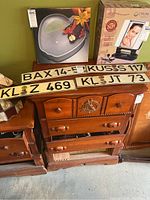 Four European license plates displayed on wooden furniture, showing codes BAX 14-5, KUS S 117, KL Z 469, KL JT 73.