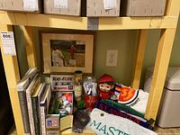 Photo showing framed golf artwork, golf towels, boxes of golf balls, books and assorted golf collectibles on a shelf.