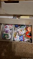 Two drawers with many assorted pins, visible text and logos related to sports and patriotic themes, including baseball teams and 'God Bless America' pin