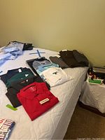 Eight men's polo shirts folded and laid on a bed, some with tags, including a red Foxfire shirt.