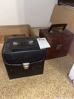 Two vintage carrying cases, one black and one brown, closed and placed on floor.