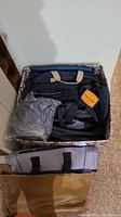 Box filled with varied tote bags in black, beige, and a packaged bag visible