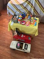 Overview of vintage toys spread on a small table with Mickey Mouse car and Ferrari model car on the floor below.