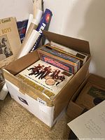 Box packed with vinyl records visible shows records upright with observable colorful album covers.