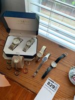 Full lot overview showing six wristwatches including two in a Geneva box with interchangeable bezels laid out on a wooden table