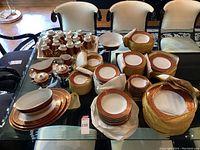 Overview of entire dinnerware and serveware set laid out on glass table.