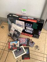 Console box, controllers, cables and games grouped on floor under lot number
