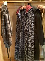 Grey plush jacket, navy and white evening cape, and black coat hanging together on a rack