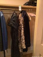 Four coats on rack from left: blue leather jacket, black patterned evening coat, leopard faux fur coat, navy faux fur coat.