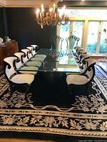 Overview of ten white upholstered dining chairs around a glass-topped table under a chandelier.