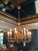 Front view of chandelier lit, showing all 18 lights and ornate scrollwork against interior setting