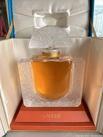 Front view of frosted crystal bottle with amber liquid and leaf motif in satin-lined box