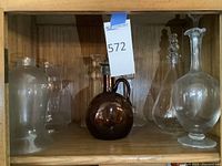 Wood cabinet shelf showing amber perfume bottle at center surrounded by clear glass decanters