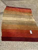 Full view of wool rug laid out on concrete showing orange and earth tone horizontal stripes.