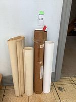 Five rolled posters in cardboard tubes standing against wall