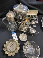 Overview of lot showing sterling silver ice bucket with lid, claret jug, candlesticks, salt and pepper shakers, and other silver items on black cloth.
