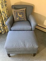 Front angled view of blue armchair with matching ottoman and decorative pillow positioned on the chair.