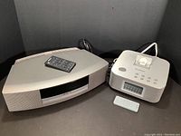 Bose Wave CD/radio player and Brookstone Bluetooth clock radio with their remotes, displayed side by side on surface