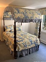 Full view of the full sized wooden canopy bed dressed in floral comforter, pillows, bedskirt, and drapes.