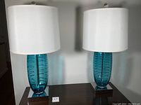 Pair of lamps side by side showing blue glass bodies, chrome bases, and white shades