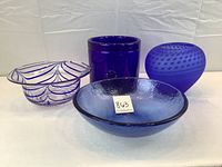 Four hand blown blue glass pieces displayed together: a patterned shallow bowl, thick ice bucket, textured vase, and shallow bowl.