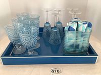Overview photo of six spiral design goblets and five wine glasses alongside ice bucket/napkin holder with napkins on blue tray