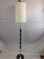 Full view of floor lamp showing tall slender structure, linen cylindrical shade, and colored glass elements on chrome shaft.