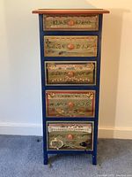 Front view of tall narrow cabinet showing five painted drawers with orange knobs.
