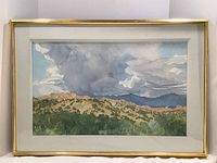 Frontal view of watercolor painting in mat and gold-tone frame showing full composition of hills, trees, and storm clouds.
